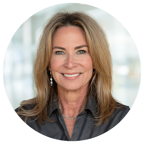 Kim Howard Jackson, President of Nurse Professionals, with shoulder-length blonde hair, in a dark blouse and necklace, smiling at the camera against a blurred light background.