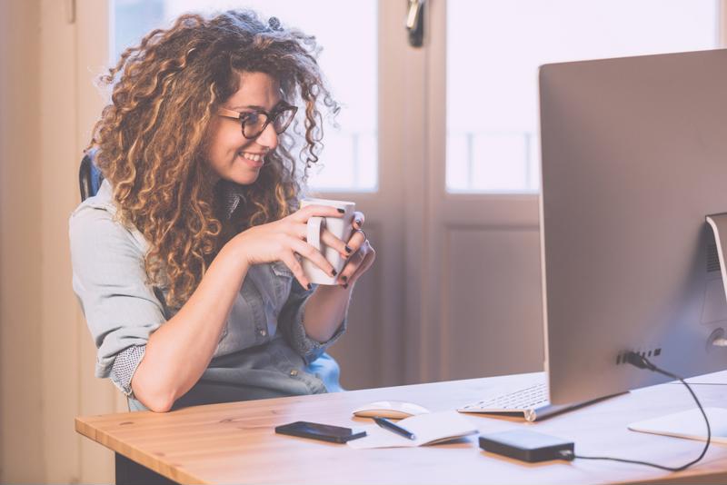 happy woman holding cup watching laptop