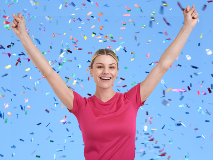 woman smiling arms raised under confetti