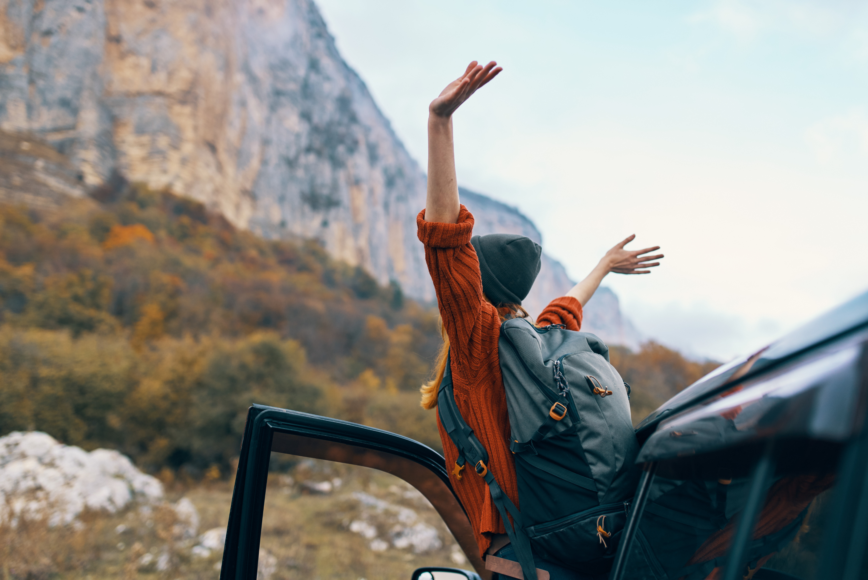 woman standing outside car with arms raised