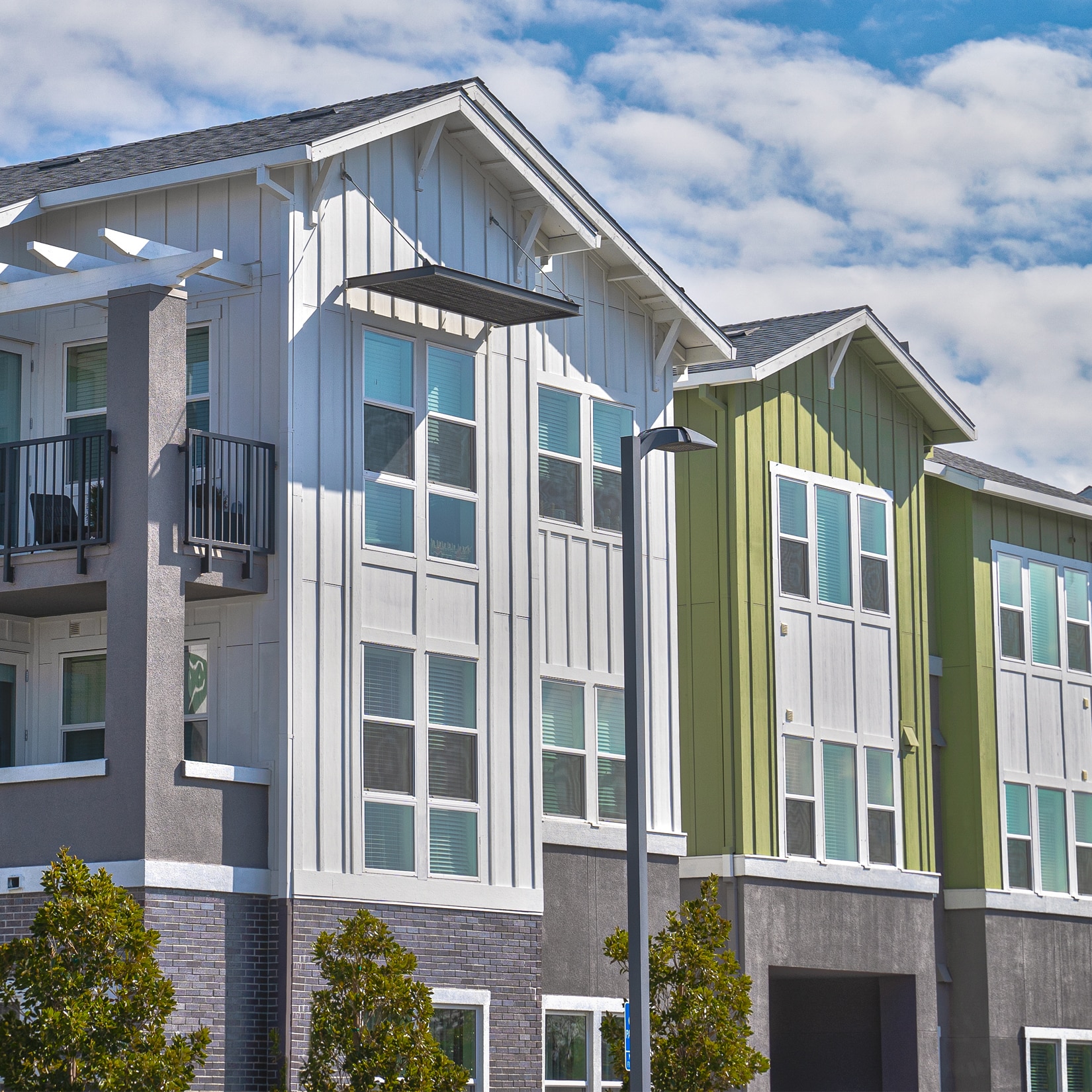 Modern apartment building with large windows and balconies, perfect for enjoying travel nurse benefits, featuring white and green siding against a partly cloudy sky.