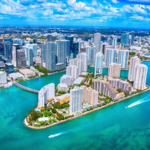 Aerial view of a coastal city with tall skyscrapers, modern buildings, green spaces, and blue water—an ideal spot for exclusive travel nurse jobs.