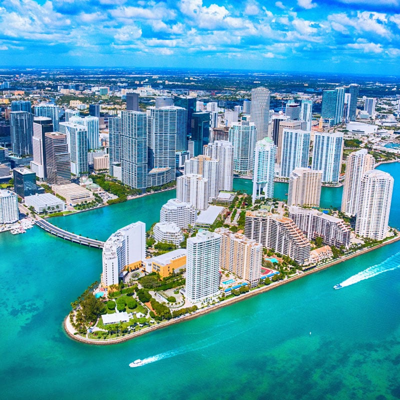 Aerial view of a coastal city with tall skyscrapers, modern buildings, green spaces, and blue water—an ideal spot for exclusive travel nurse jobs.