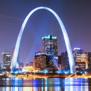 The Gateway Arch in St. Louis shines at night as city lights reflect on the water—a stunning view for those seeking exclusive travel nurse jobs nearby.