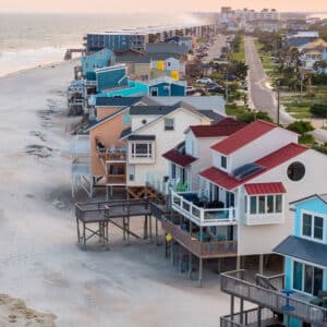 A row of colorful beach houses on stilts lines the shore next to a road, offering scenic views perfect for those seeking exclusive travel nurse jobs by the ocean.