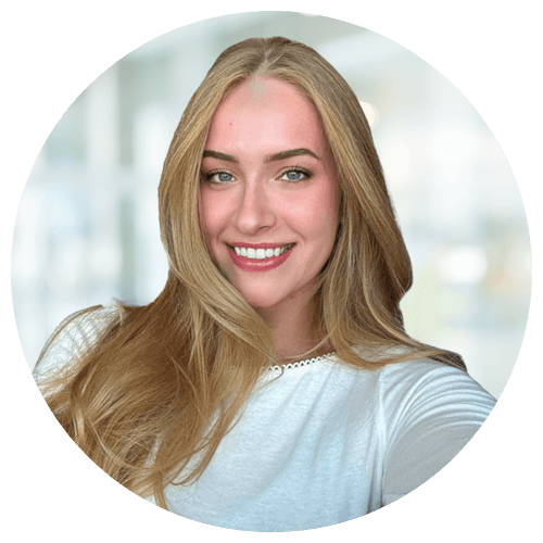 A young woman with long blonde hair and a white top smiles at the camera against a blurred light background.