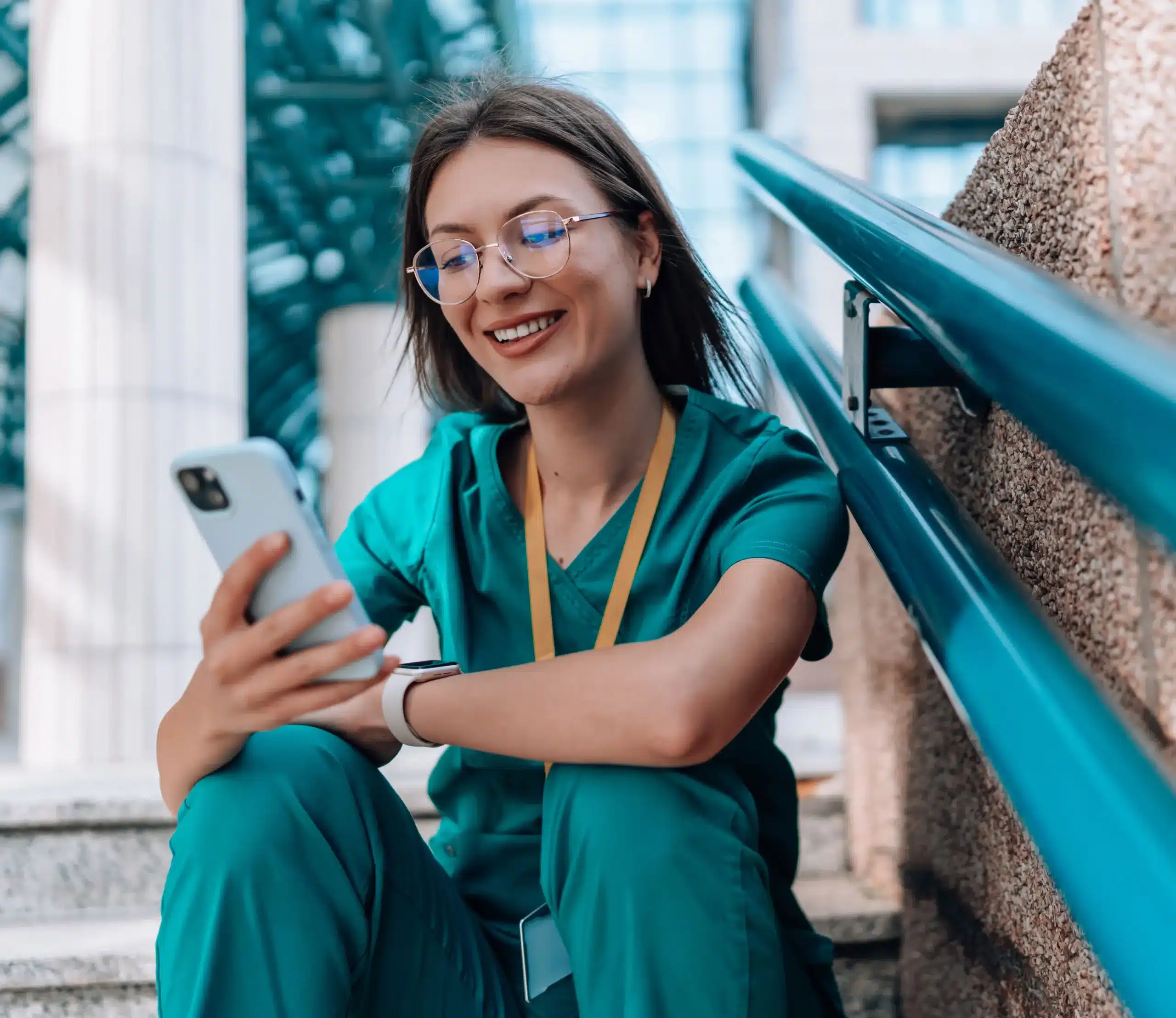 Female nurse sitting on stairs outside looking at smart phone