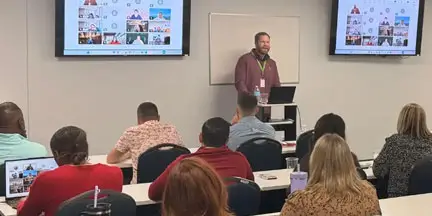Healthcare professionals attend a training session with a presenter demonstrating information on presentation screens.