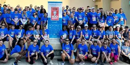 Large group of participants in matching blue event shirts posing together around a central event sign.